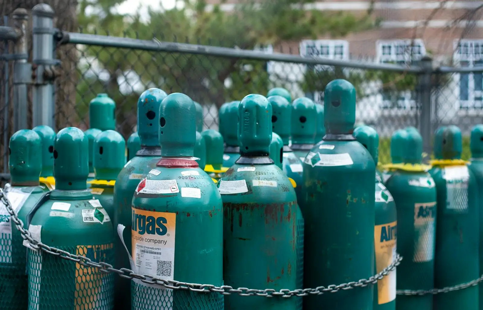 Rows of teal gas cylinders securely chained, emphasizing industrial safety outdoors.