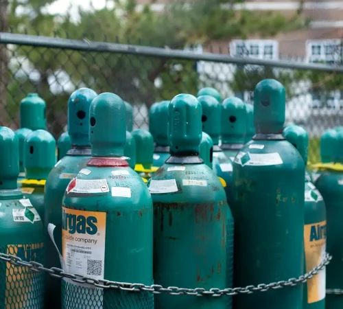 Rows of teal gas cylinders securely chained, emphasizing industrial safety outdoors.