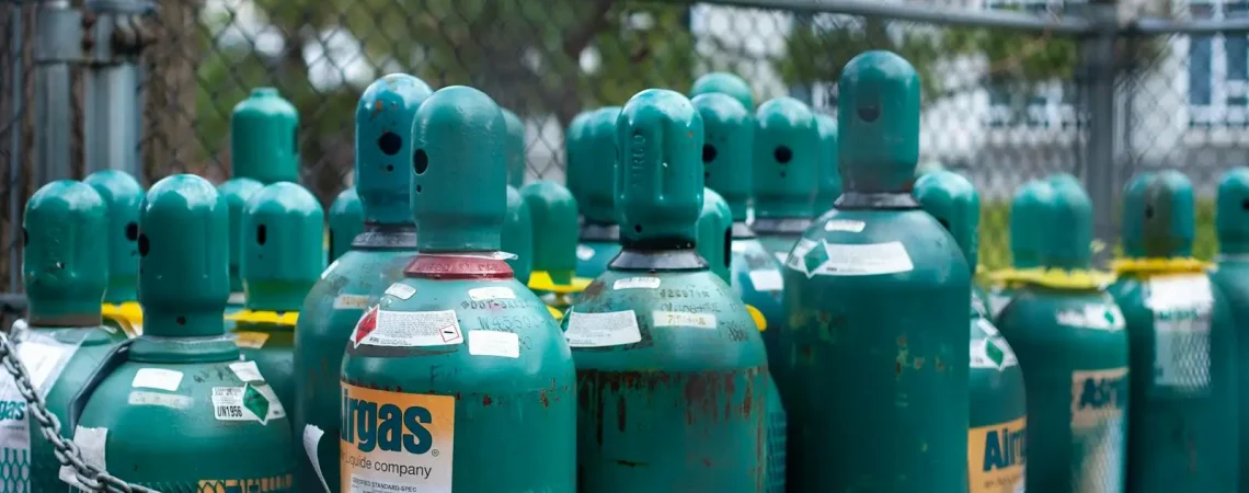 Rows of teal gas cylinders securely chained, emphasizing industrial safety outdoors.